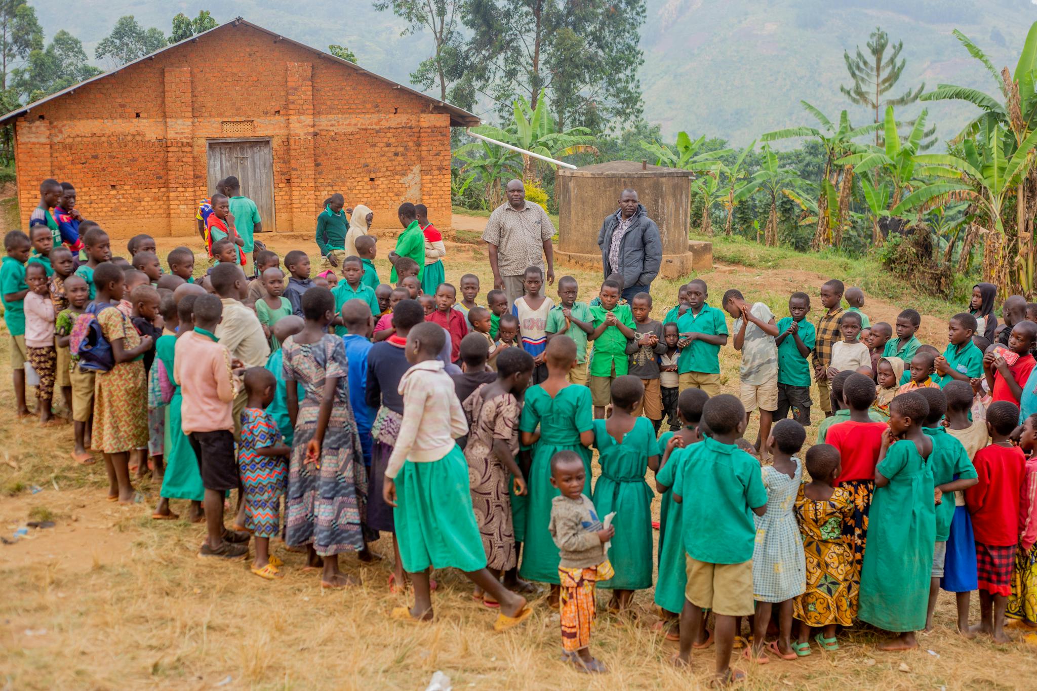 A large group of children gather outside a rural schoolhouse in Africa.